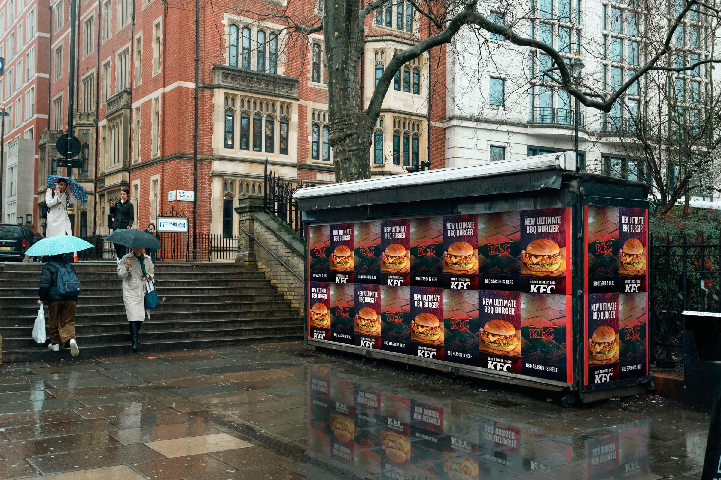 KFC BBQ Burger posters tiled across a street kiosk on a wet London street