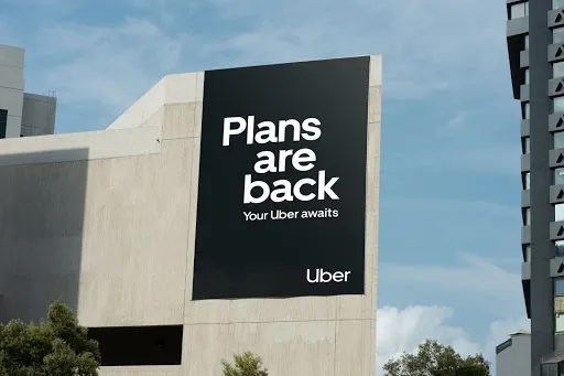 Uber "plans are back" billboard on a concrete building against blue sky