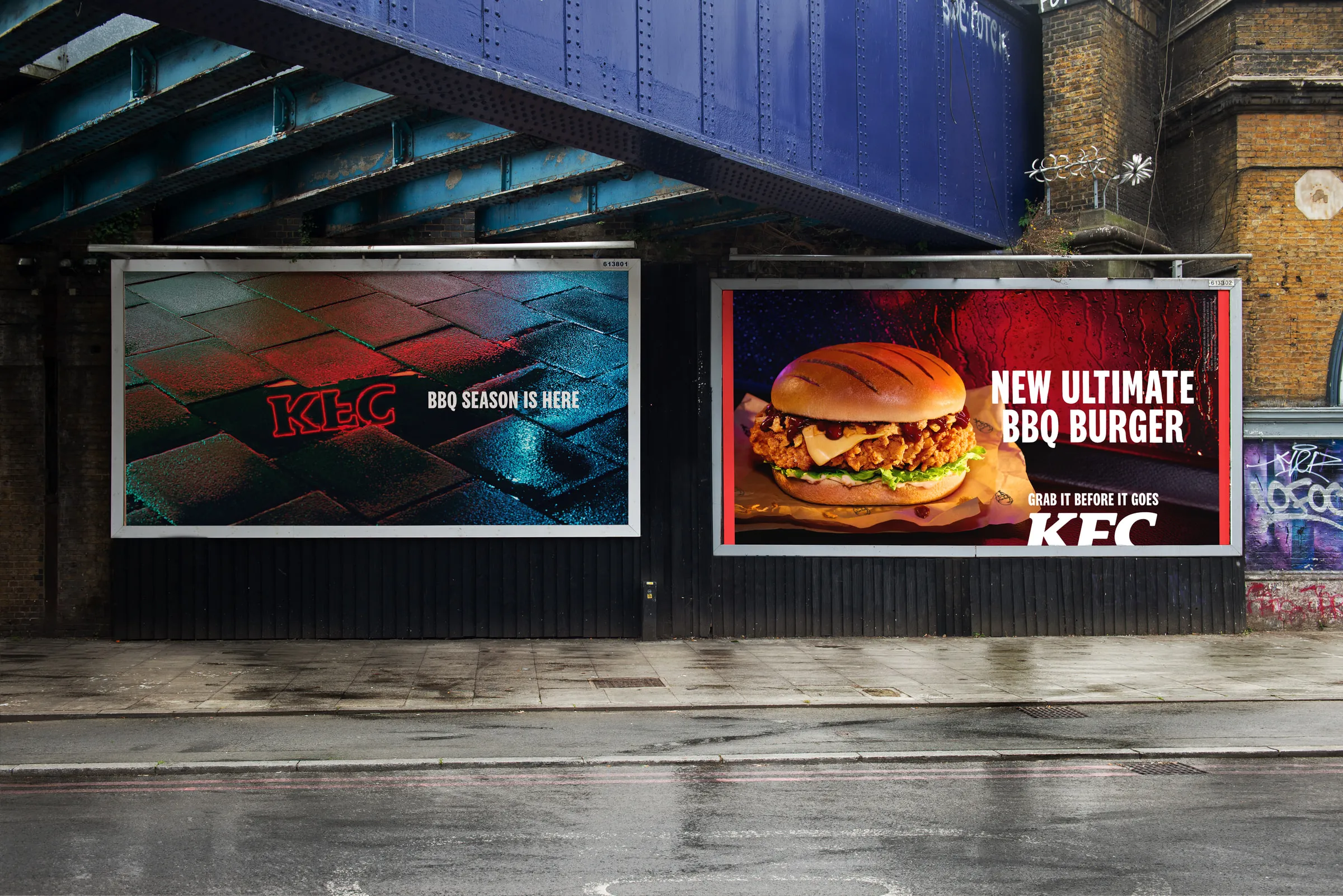 KFC BBQ season billboards beneath a blue railway bridge on a rain-soaked street