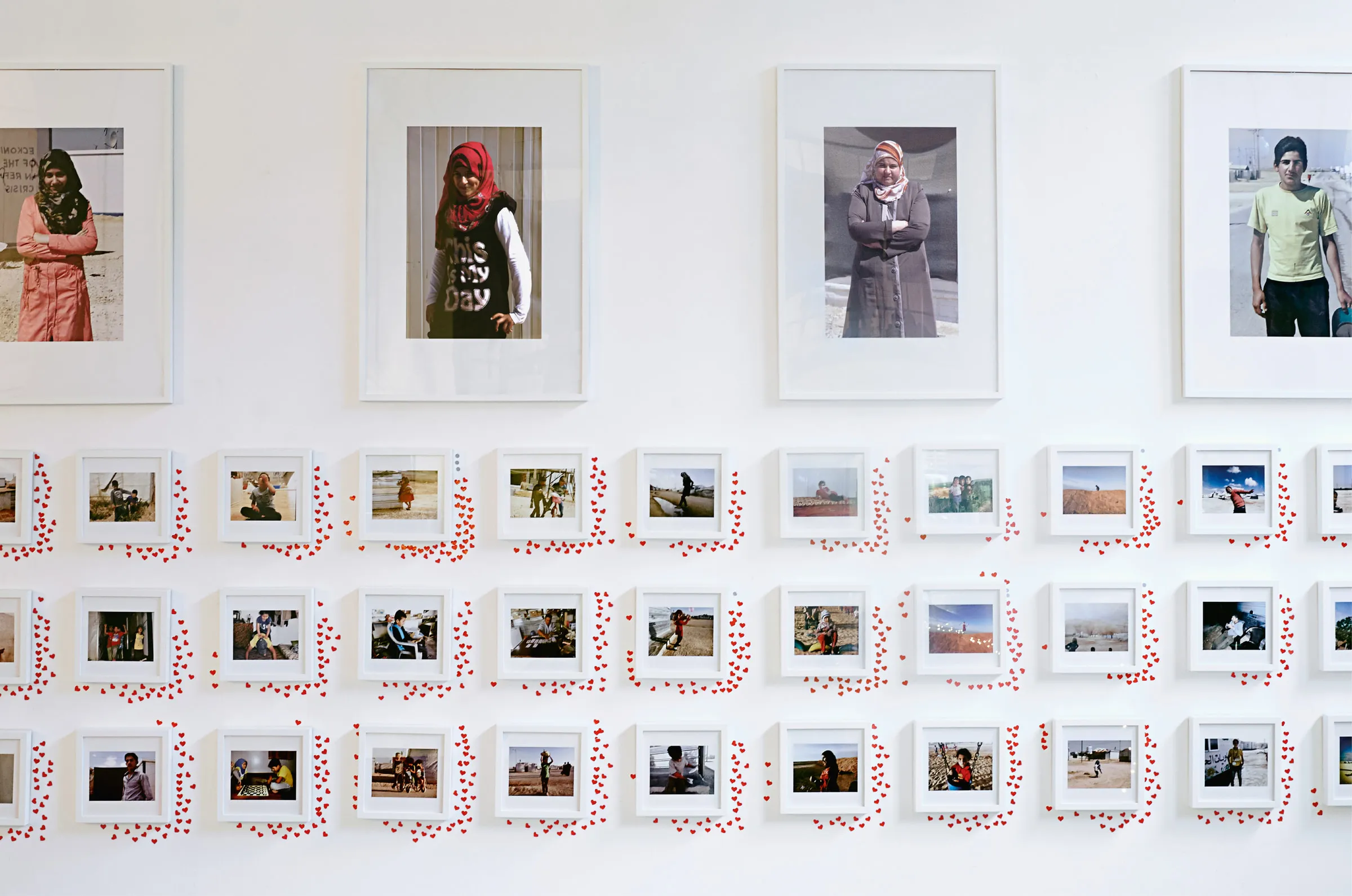 Wall of the children's photographs, red heart stickers clustered around the most-liked frames