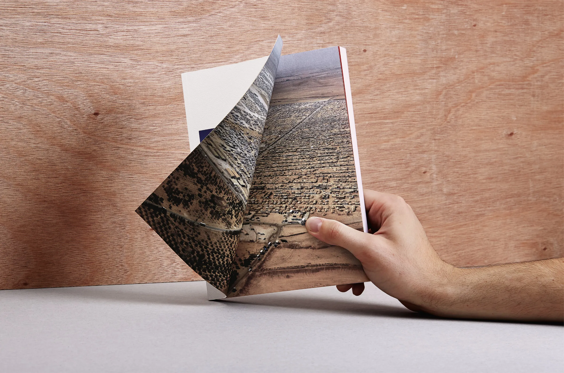 Hand opening the book on an aerial spread of the Za'atari camp